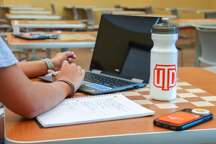 Student using a laptop. A UTD-themed water bottle is visible.