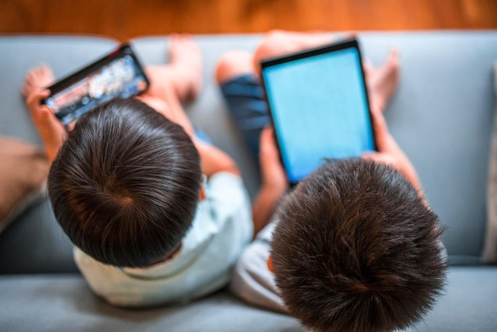 Two children, one with a cell phone and one with a tablet.