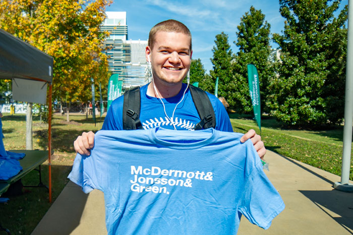 Student holding up a blue t-shirt that reads McDermott and Jonsson and Green